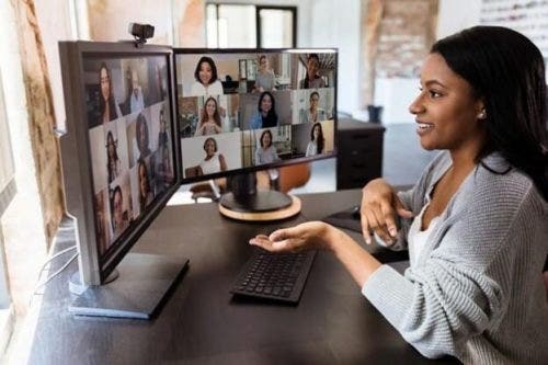 A smiling worker engages with co-workers via videoconference on a monitor.